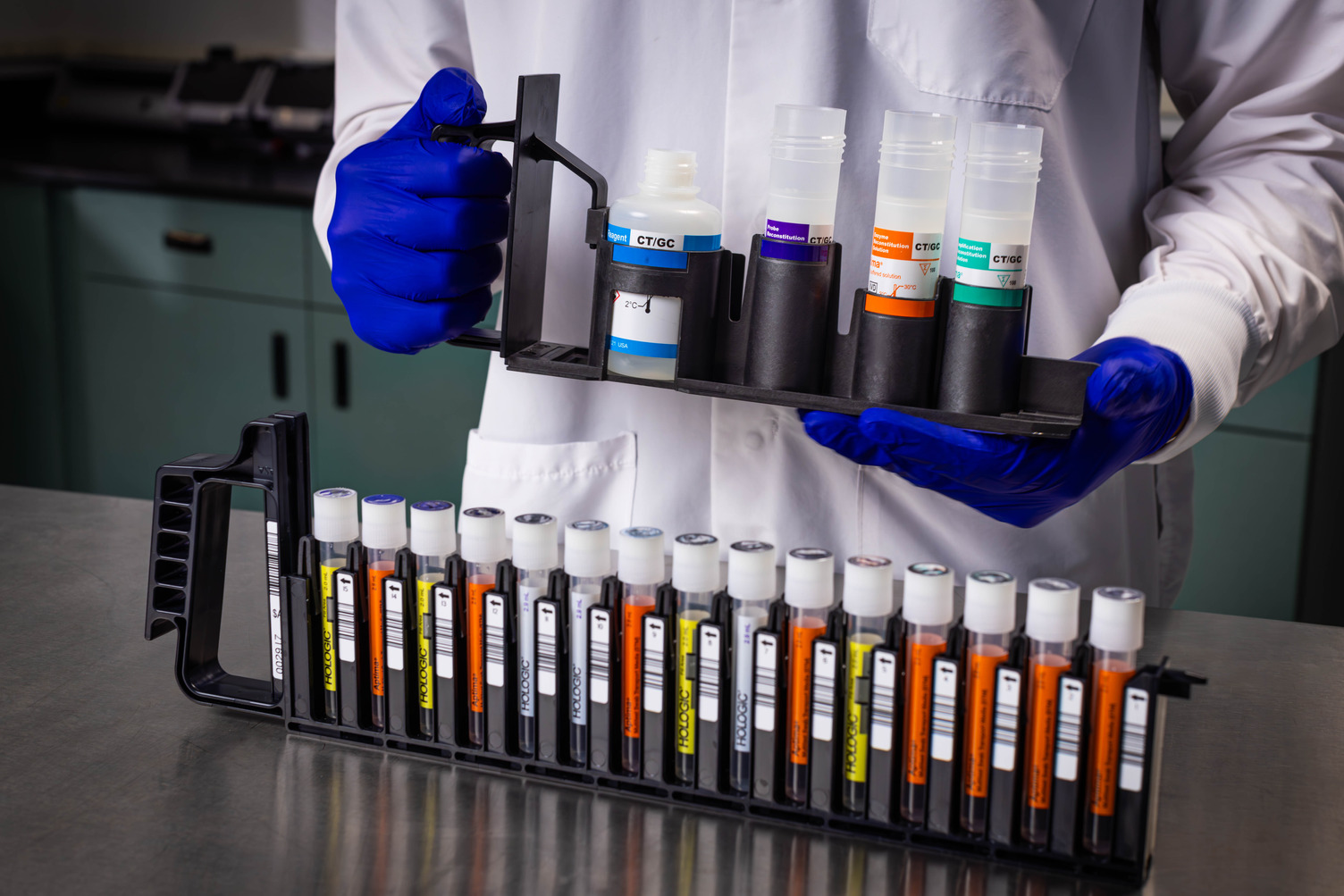 Lab Tech Holding Aptima Reagent Rack Next to Aptima Rack on Table