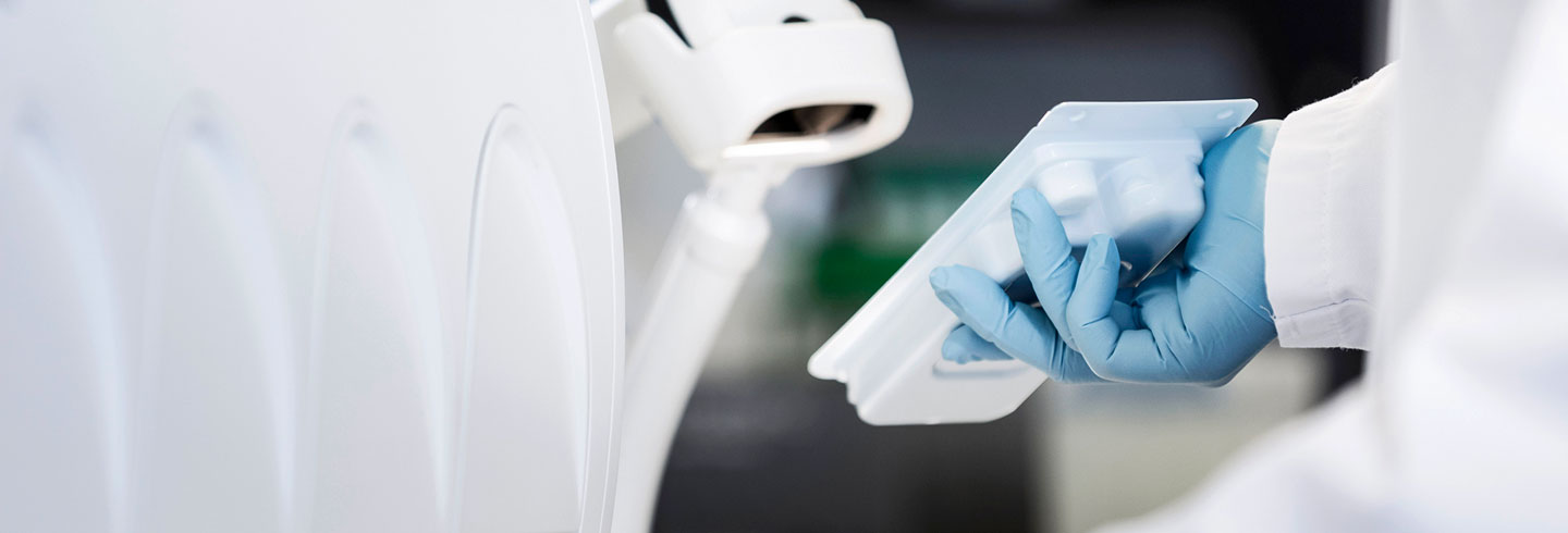 Gloved hand holding small tray in lab setting.