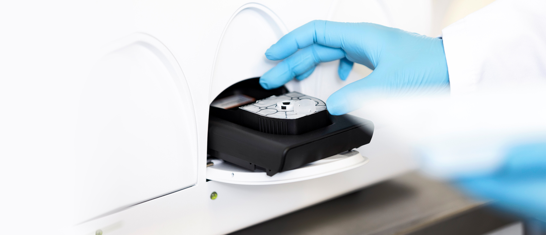 Gloved hand presses button on machine in lab setting.