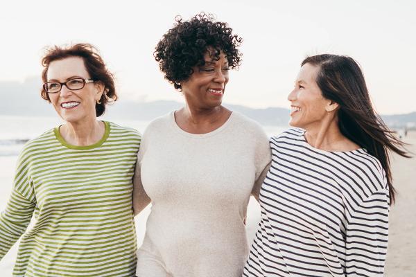 Three women smiling and walking on the beach together.