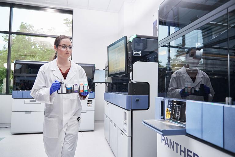 Female lab technician carrying a tray of specimens to insert into Panther system