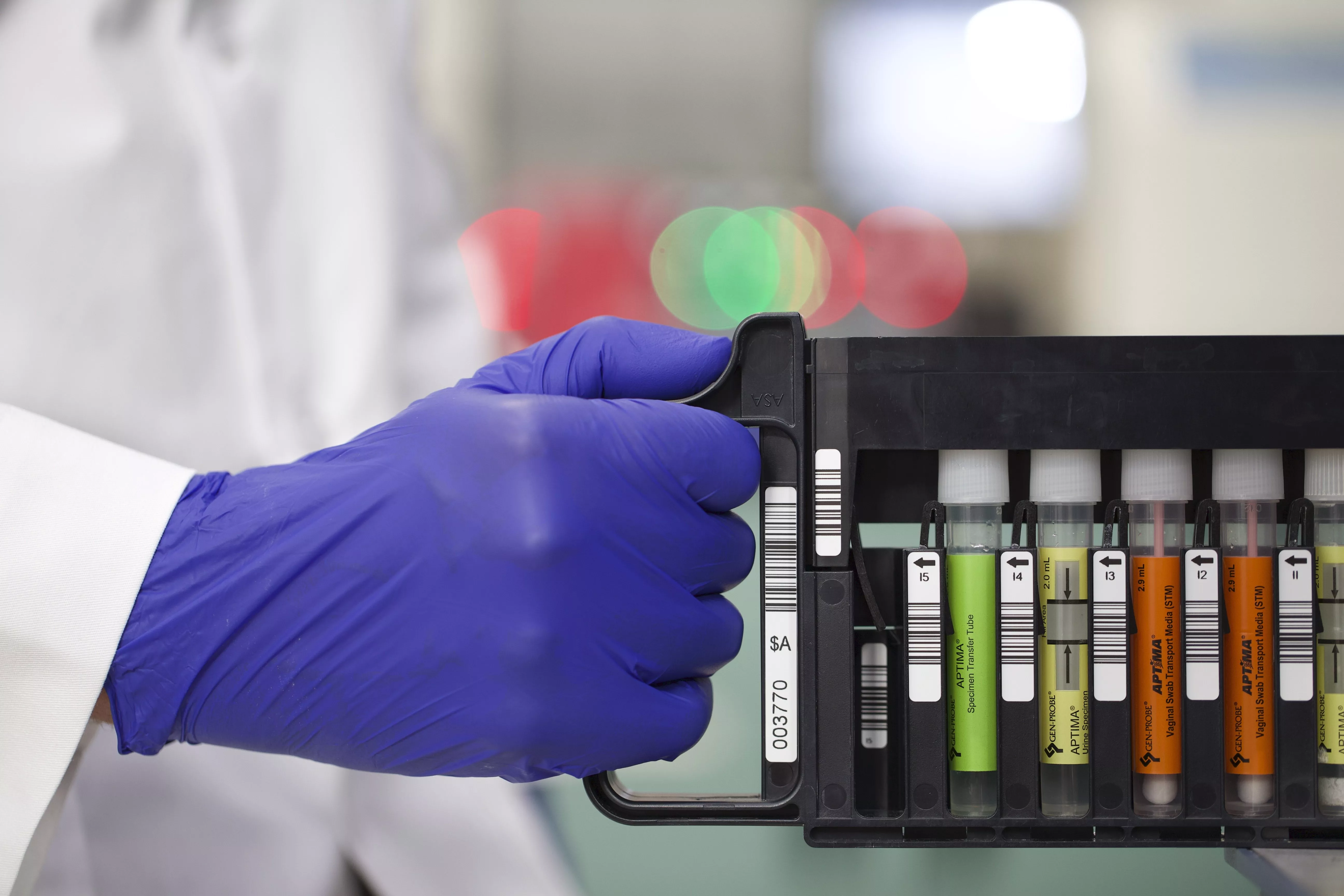 Gloved hand holding vial rack in a lab setting