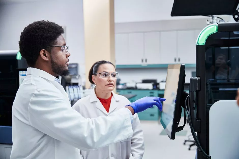 Technician pointing at monitor of medical system in lab setting