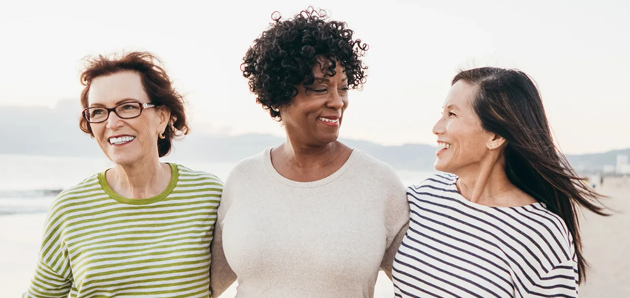 Three women smiling and walking on the beach together.