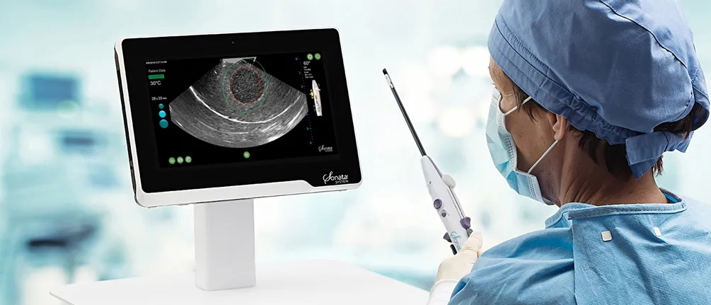 Surgeon holding NovaSure instrument with patient on hospital bed in background