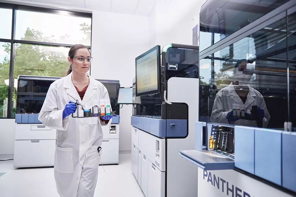 Lab technician carrying a tray of specimens to insert into Panther system