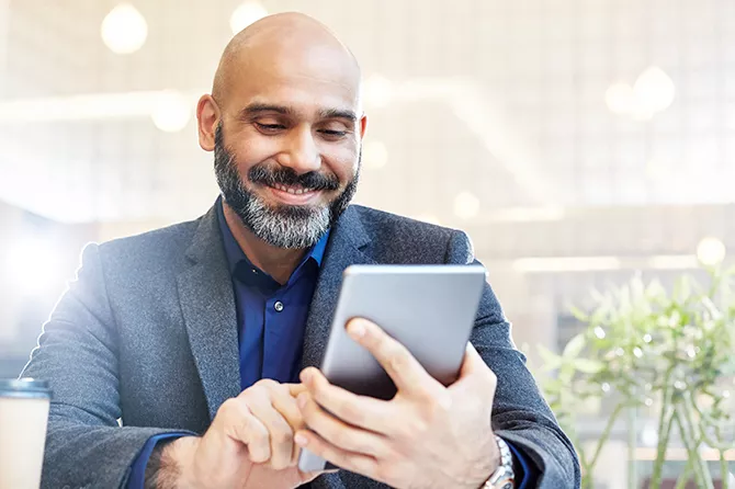 Man smiles while interacting with a tablet device in an outdoor setting