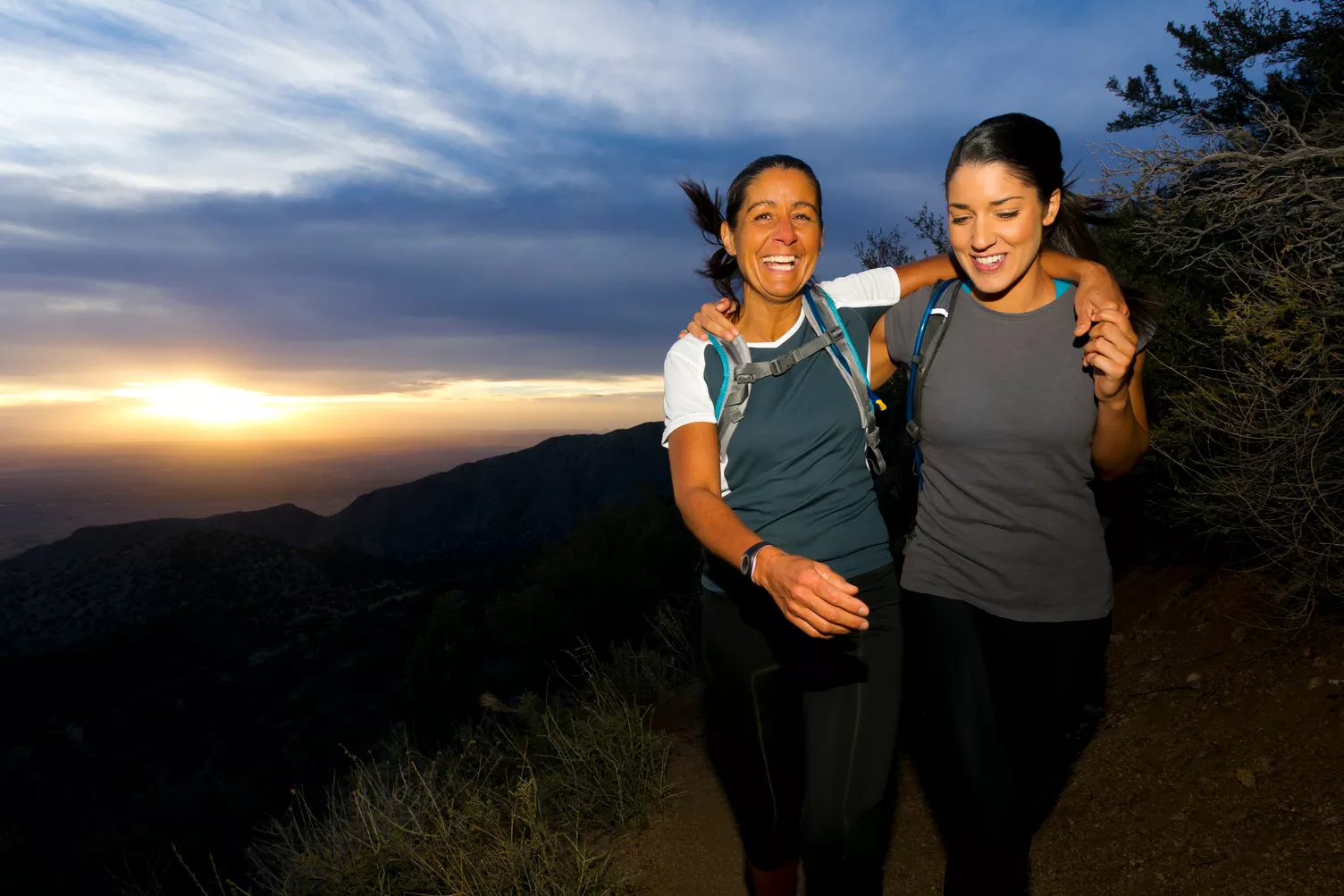 Two women hiking along a hill at sunset.