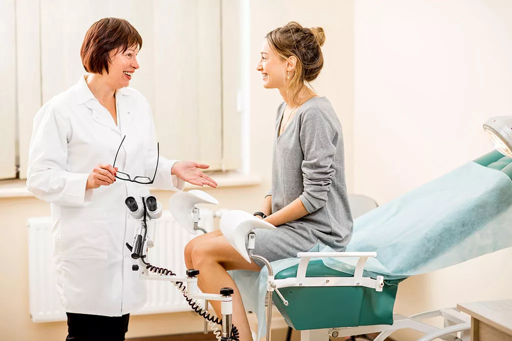 Female patient sitting on hospital examination table talking to healthcare professional