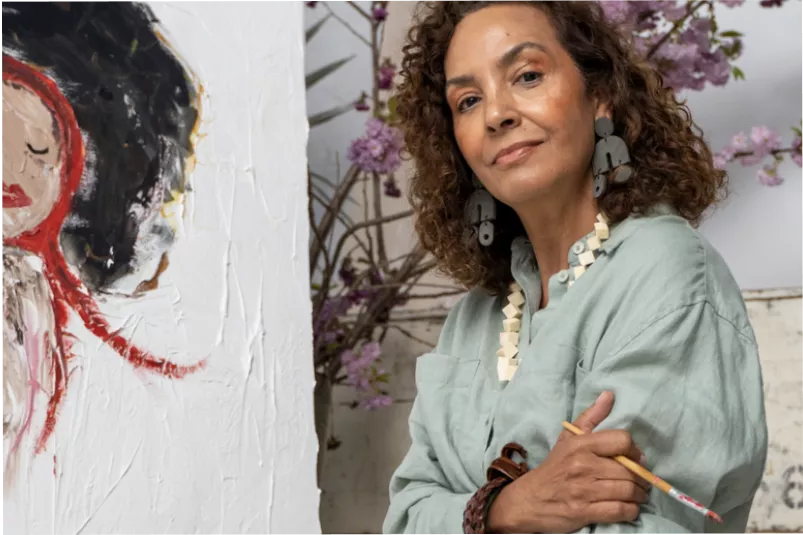 Confident female artist holding brush in front of painting
