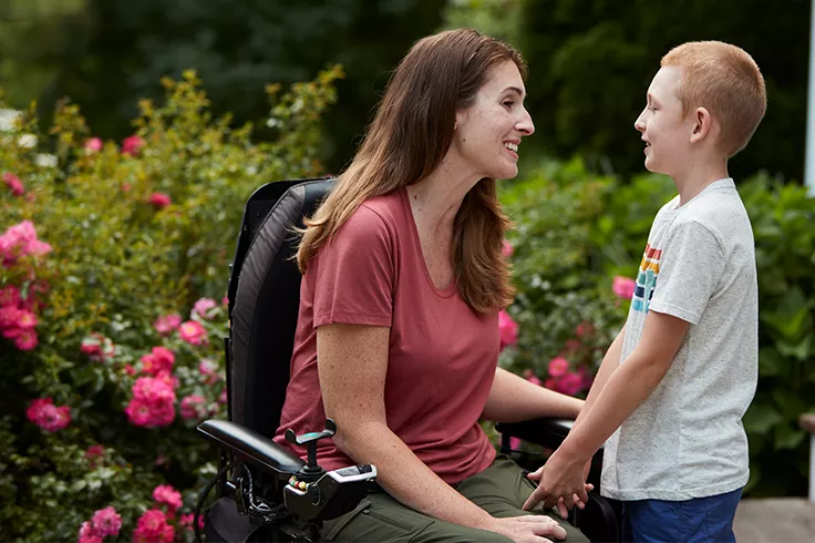 Woman sitting on wheelchair and smiling with boy in outdoor setting